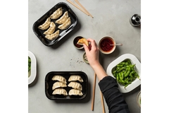 A hand using chopsticks grabbing for dumplings on a tray.